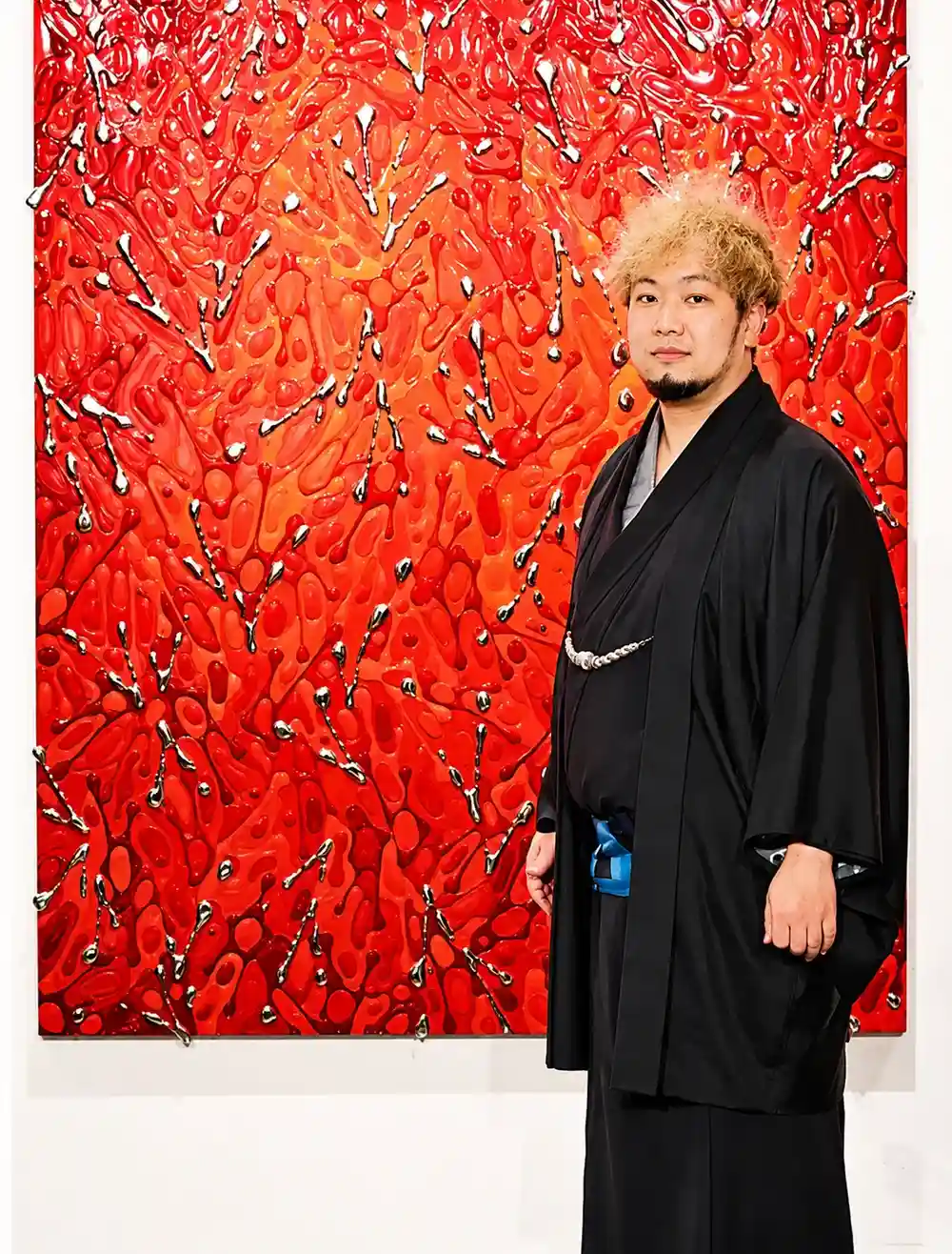 現代アーティスト 池内信介（Shinsuke Ikeuchi）。赤い樹脂と純錫の作品の前に立つ